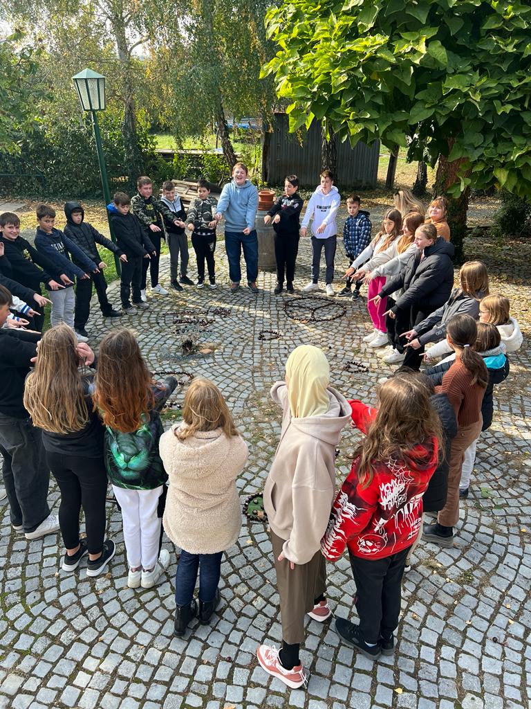 Religion und soziales Lernen. Kinder legen mit Naturmaterialien (Kastanien) das Wort Frieden auf und machen ein Friedenszeichen